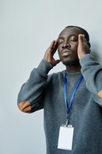 Un jeune homme en pull se tient la tête, exprimant le stress et l'épuisement.