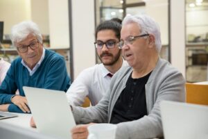 Trois hommes collaborent et apprennent la technologie ensemble sur des ordinateurs portables à l'intérieur.