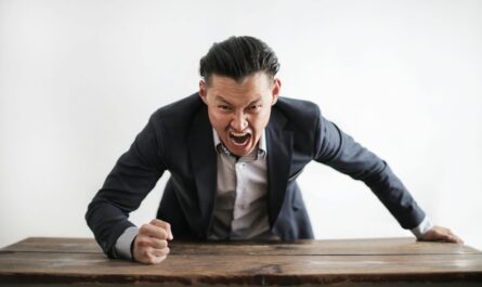 Homme d'affaires expressif en colère en costume formel regardant la caméra et criant de folie tout en frappant le bureau avec le poing