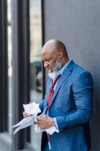 Vue latérale d'un entrepreneur afro-américain agressif lisant des documents et froissant du papier tout en se tenant près d'un bâtiment dans la rue de la ville