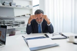 Un homme d'affaires âgé en costume semble stressé alors qu'il est assis à un bureau avec des documents dans un bureau.
