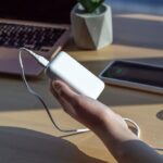 Un homme qui utilise un "chargeur usb portable pour voyage" pour recharger son téléphone, un exemple d'une utilisation moderne et efficace pour les voyageurs.