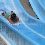 Enfant en maillot vert glisse sur un toboggan aquatique bleu dans une piscine de camping