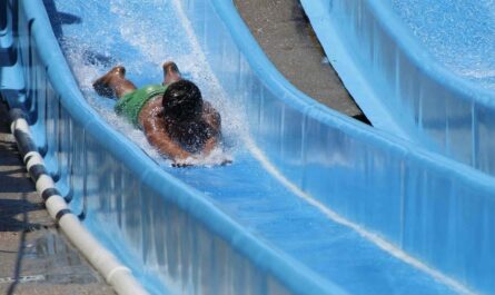 Enfant en maillot vert glisse sur un toboggan aquatique bleu dans une piscine de camping