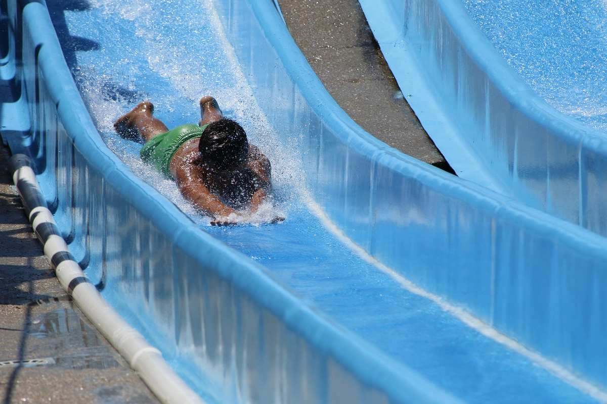 Enfant en maillot vert glisse sur un toboggan aquatique bleu dans une piscine de camping